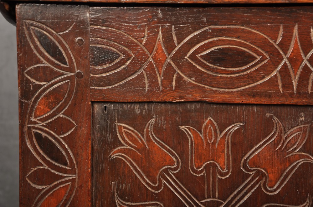 A 17th-century dark stained oak coffer with carved tulip panels and geometric border details. View VI