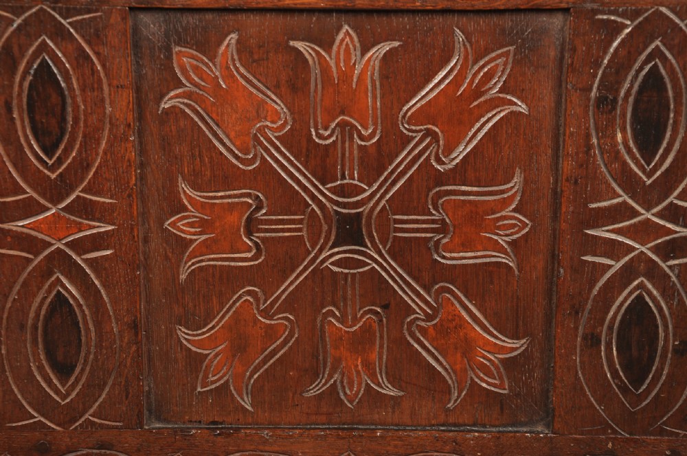 A 17th-century dark stained oak coffer with carved tulip panels and geometric border details. View VII