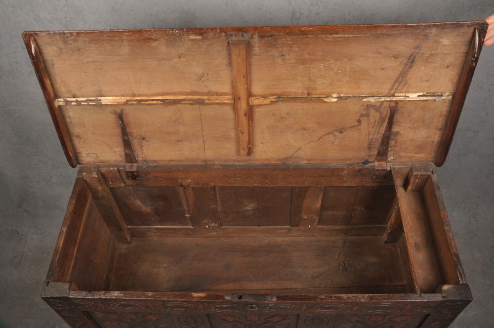 A 17th-century dark stained oak coffer with carved tulip panels and geometric border details. View VIII