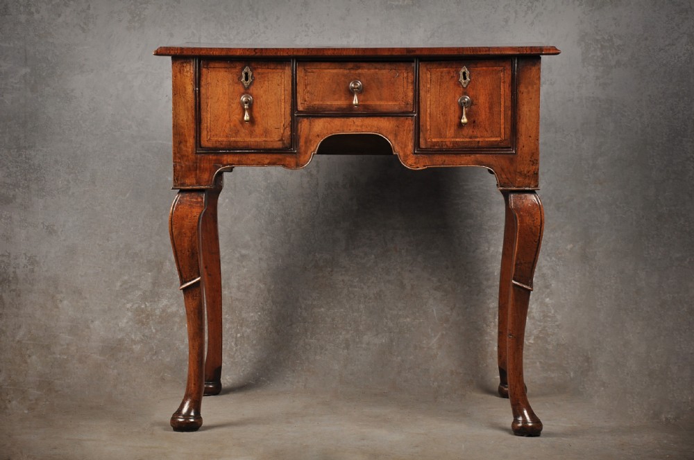 An 18th-century walnut lowboy table featuring three drawers with brass drop handles, a shaped lower apron, and cabriole legs.