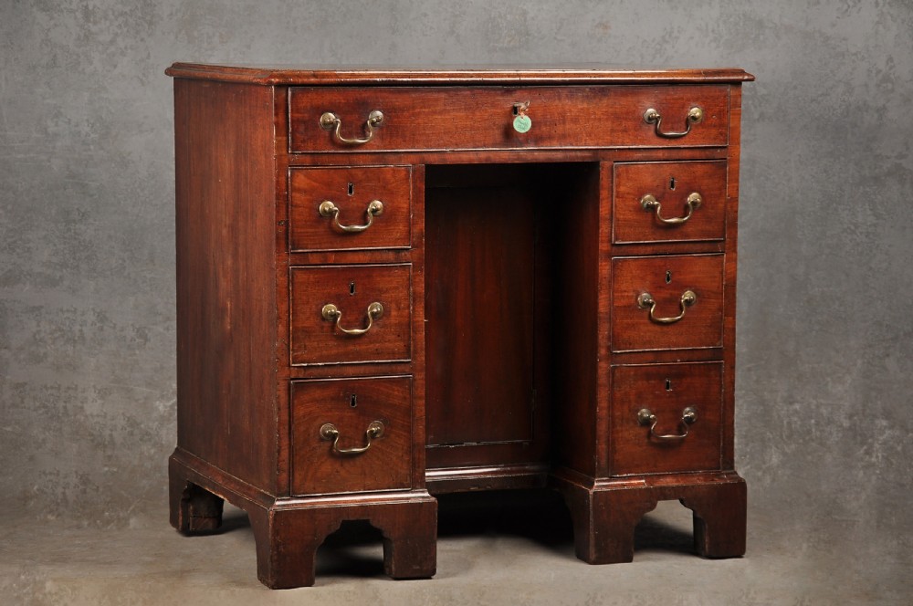 A mid-18th-century mahogany kneehole desk featuring a long upper drawer, six small side drawers, brass handles, and a central recessed cupboard on bracket feet.