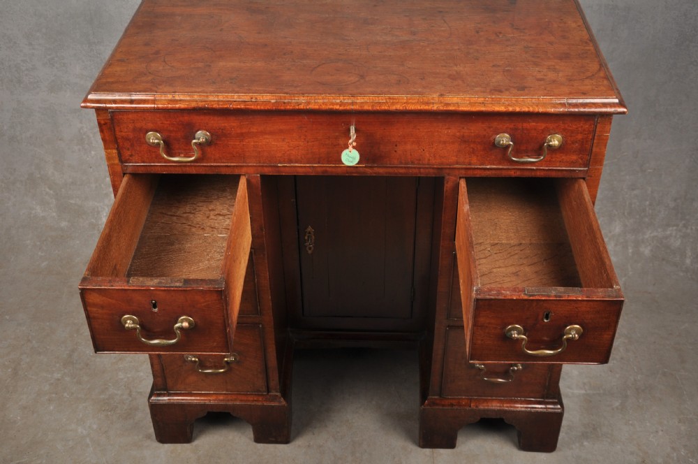A mid-18th-century mahogany kneehole desk featuring a long upper drawer, six small side drawers, brass handles, and a central recessed cupboard on bracket feet. View V