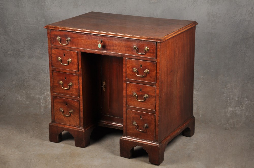 A mid-18th-century mahogany kneehole desk featuring a long upper drawer, six small side drawers, brass handles, and a central recessed cupboard on bracket feet. View XII