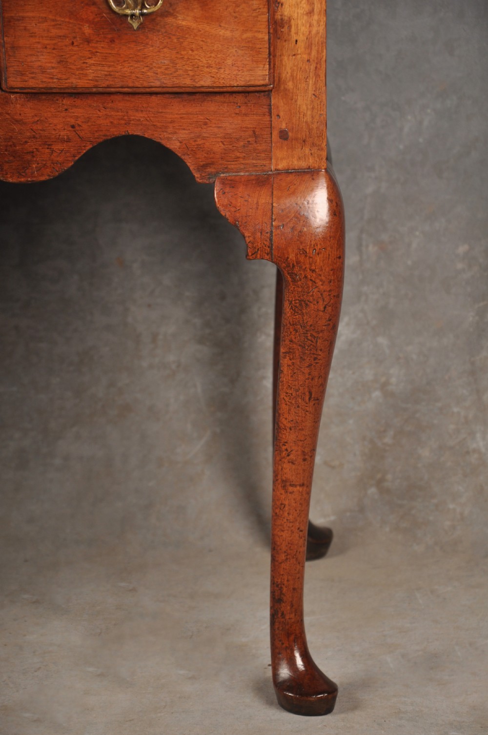 An early 18th-century red walnut lowboy table featuring three drawers with brass handles, a scalloped apron, and four cabriole legs on pad feet. View III