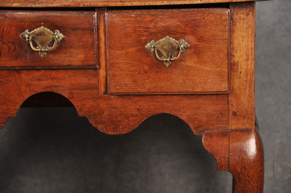 An early 18th-century red walnut lowboy table featuring three drawers with brass handles, a scalloped apron, and four cabriole legs on pad feet. View IV