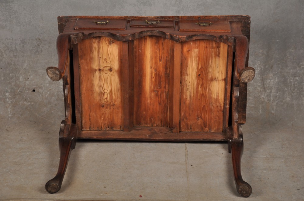 An early 18th-century red walnut lowboy table featuring three drawers with brass handles, a scalloped apron, and four cabriole legs on pad feet. View X