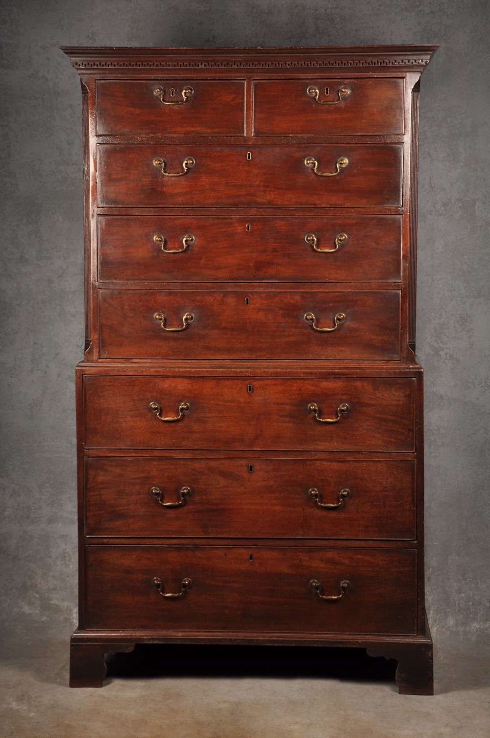 An 18th-century Georgian mahogany tallboy chest-on-chest featuring two stacked sections with brass swan-neck handles, dentil moulding, fluted canted corners, and bracket feet.