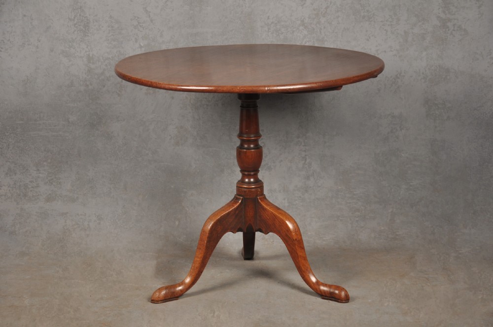 An 18th-century mahogany tripod table with a circular top supported by a turned central stem and three splayed cabriole legs with pad feet.