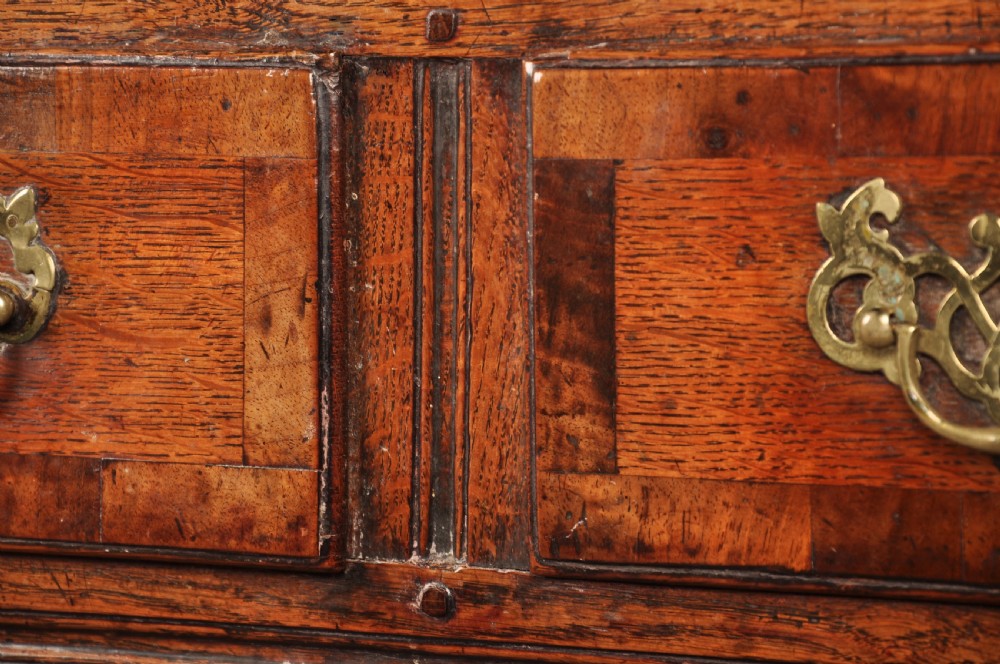 An early 18th-century dark oak dresser base featuring fielded panel cupboard doors, multiple drawers, and brass backplate handles. View VII