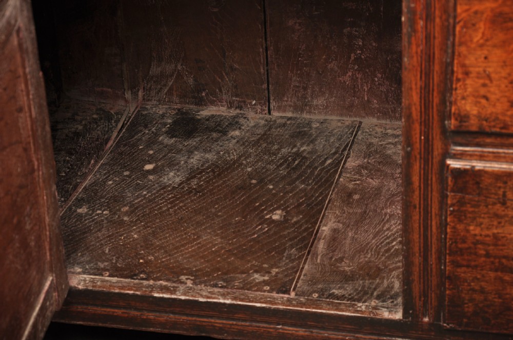 An early 18th-century dark oak dresser base featuring fielded panel cupboard doors, multiple drawers, and brass backplate handles. View X