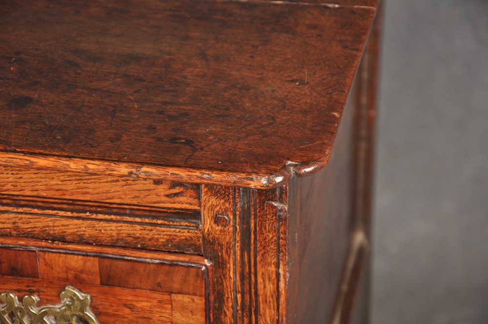 An early 18th-century dark oak dresser base featuring fielded panel cupboard doors, multiple drawers, and brass backplate handles. View XIV