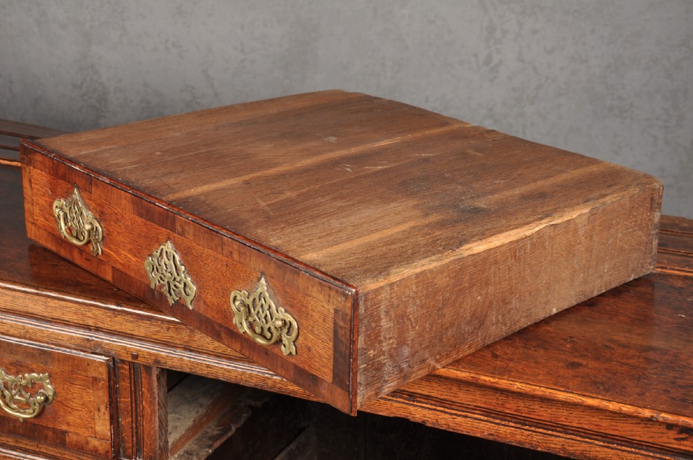 An early 18th-century dark oak dresser base featuring fielded panel cupboard doors, multiple drawers, and brass backplate handles. View XVI
