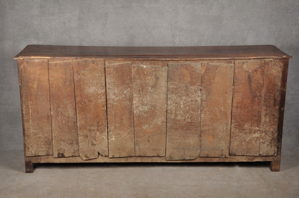 An early 18th-century dark oak dresser base featuring fielded panel cupboard doors, multiple drawers, and brass backplate handles. View XVII