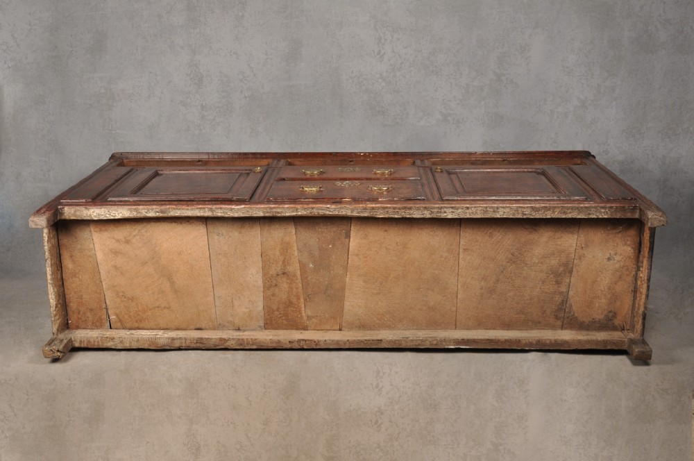 An early 18th-century dark oak dresser base featuring fielded panel cupboard doors, multiple drawers, and brass backplate handles. View XVIII