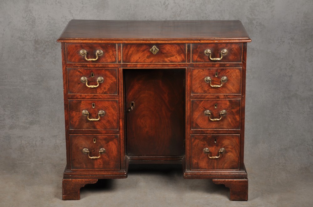 An 18th-century Georgian mahogany kneehole desk featuring brass swan-neck handles, a central recessed cupboard, and bracket feet.