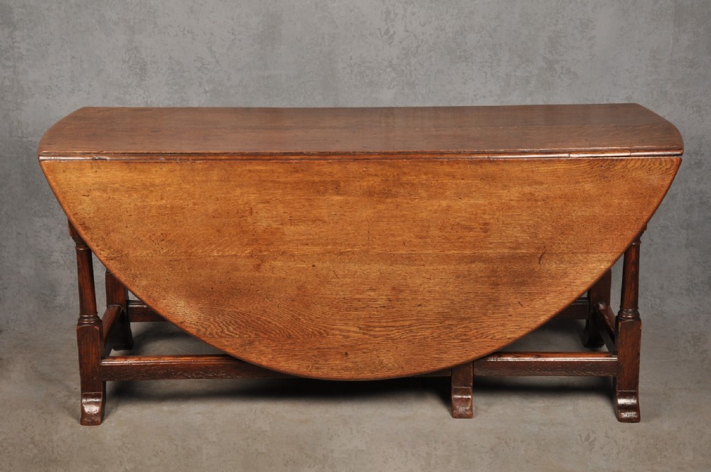 A large 18th-century oak gateleg table shown with one semi-circular drop leaf folded down and turned legs resting on rectangular stretchers.
