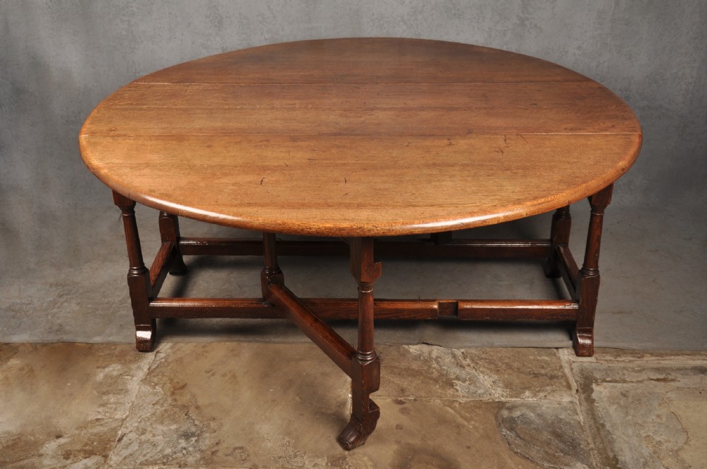 A large 18th-century oak gateleg table shown with one semi-circular drop leaf folded down and turned legs resting on rectangular stretchers. View II