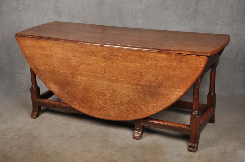 A large 18th-century oak gateleg table shown with one semi-circular drop leaf folded down and turned legs resting on rectangular stretchers. View X