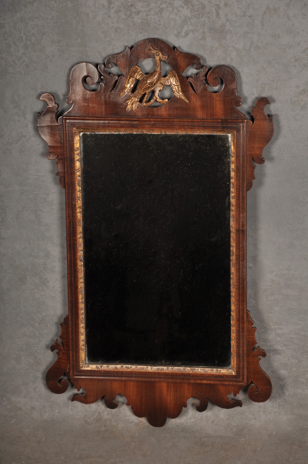 An 18th-century Chippendale mahogany wall mirror featuring a scrollwork fretwork frame, an inner gilt slip, and a carved gilt phoenix motif atop the cresting.