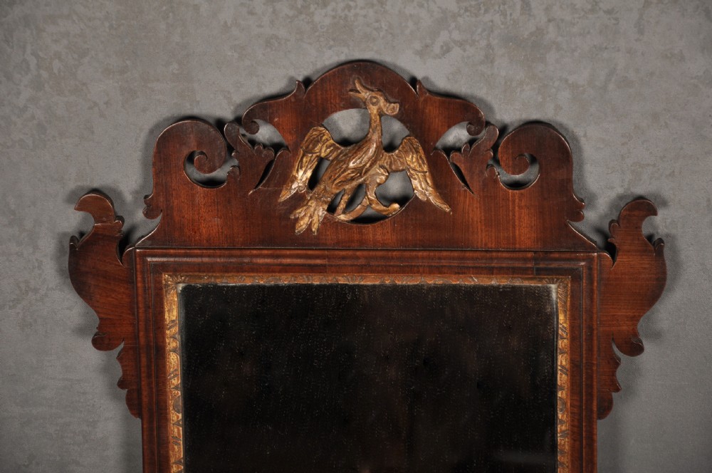 An 18th-century Chippendale mahogany wall mirror featuring a scrollwork fretwork frame, an inner gilt slip, and a carved gilt phoenix motif atop the cresting. View II