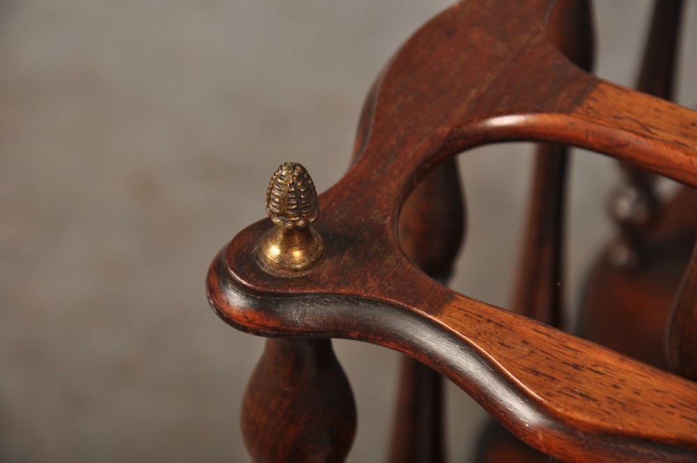 An early nineteenth-century dark rosewood Canterbury music stand featuring vertical spindle dividers, a brass central handle, a lower tier, turned legs, and brass castors. View IV