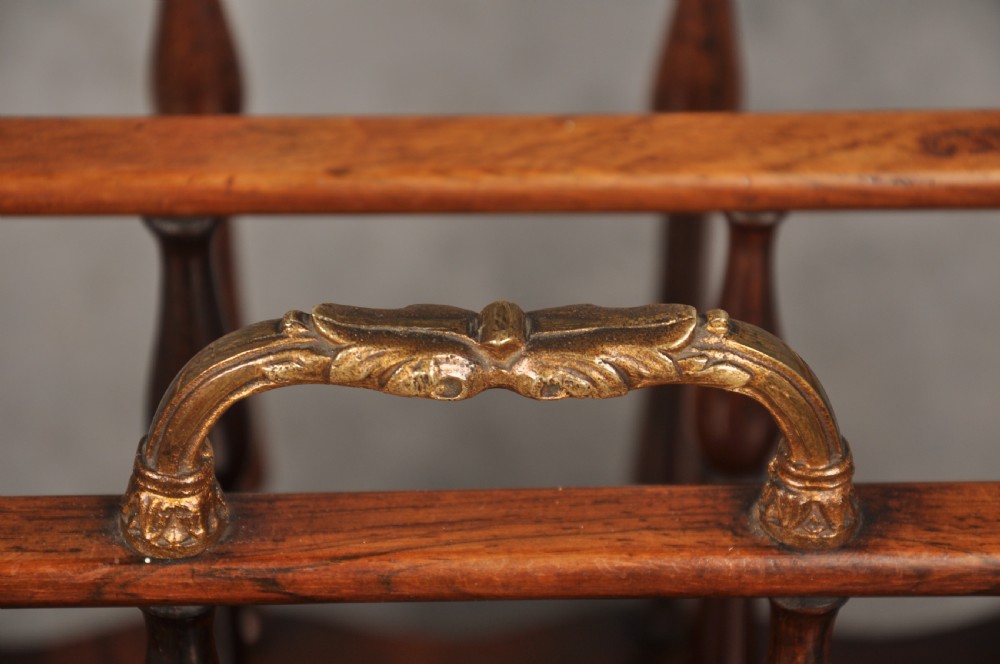 An early nineteenth-century dark rosewood Canterbury music stand featuring vertical spindle dividers, a brass central handle, a lower tier, turned legs, and brass castors. View V