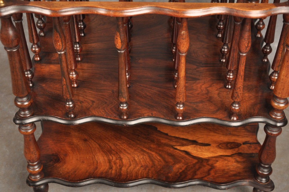 An early nineteenth-century dark rosewood Canterbury music stand featuring vertical spindle dividers, a brass central handle, a lower tier, turned legs, and brass castors. View VI