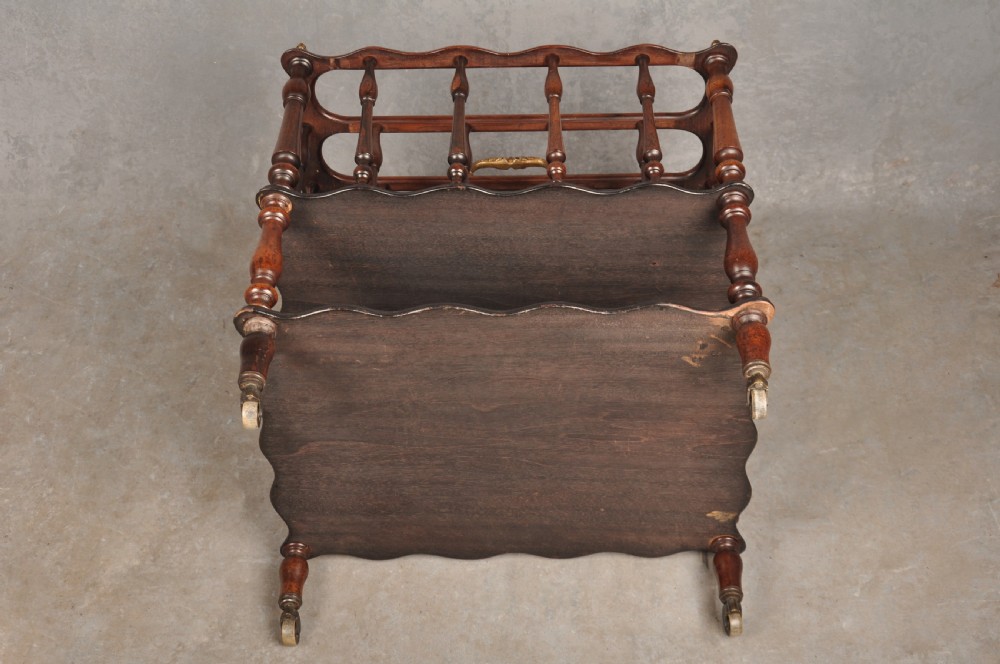 An early nineteenth-century dark rosewood Canterbury music stand featuring vertical spindle dividers, a brass central handle, a lower tier, turned legs, and brass castors. View VII