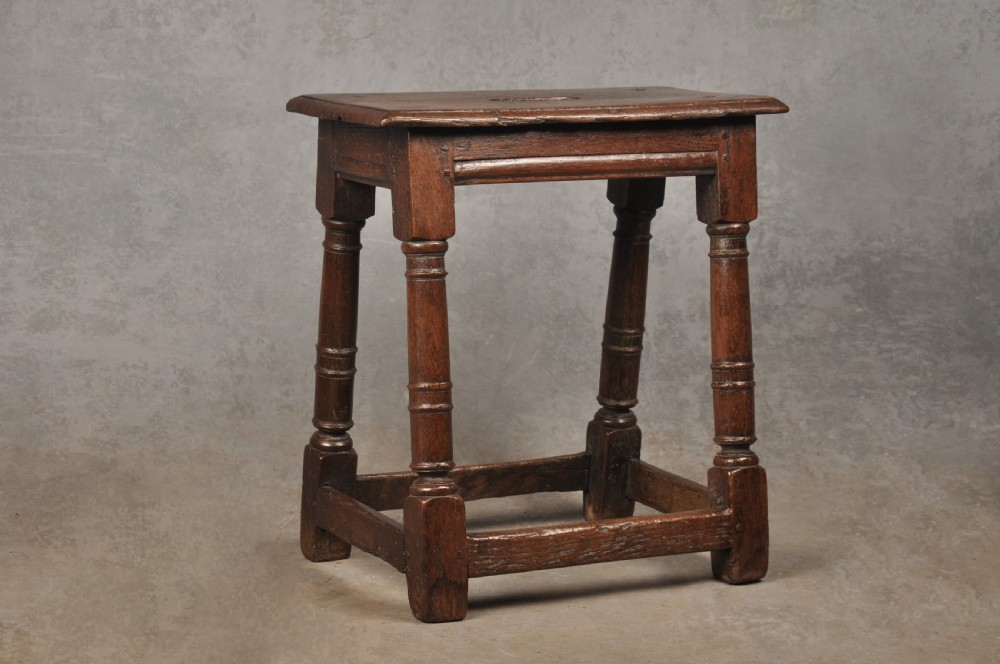 A 17th-century oak joint stool with turned legs, mortise-and-tenon peg construction, and lower perimeter stretchers.