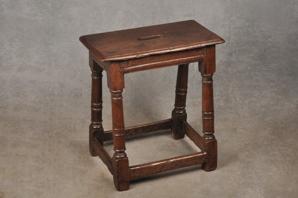 A 17th-century oak joint stool with turned legs, mortise-and-tenon peg construction, and lower perimeter stretchers. View X