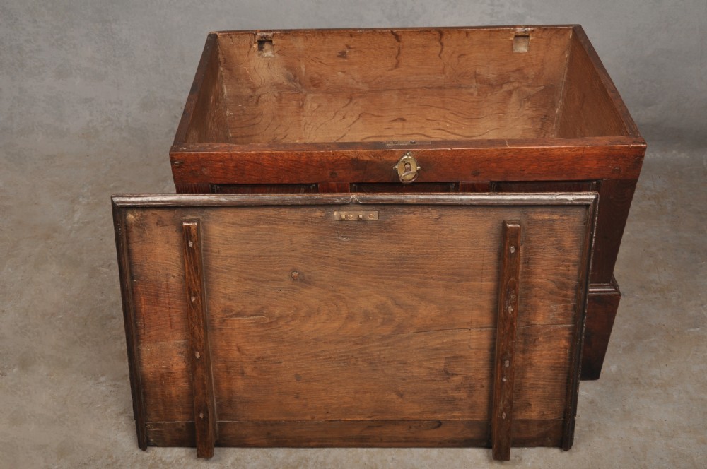 An 18th-century dark oak coffer bach with a hinged lid, three front panels, two lower drawers, and brass handles. View V