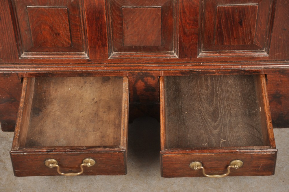 An 18th-century dark oak coffer bach with a hinged lid, three front panels, two lower drawers, and brass handles. View VII