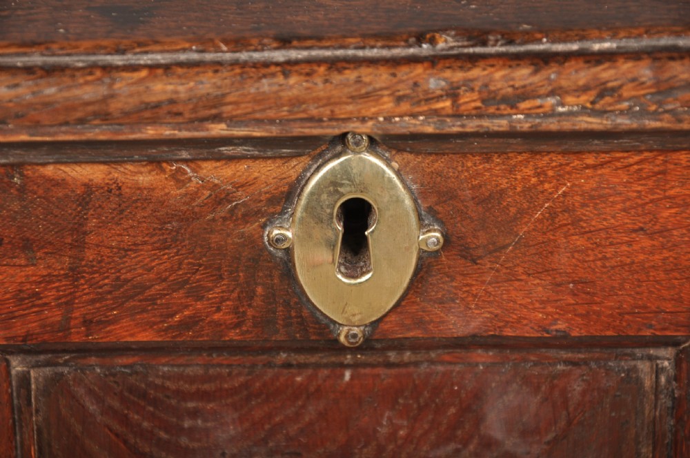 An 18th-century dark oak coffer bach with a hinged lid, three front panels, two lower drawers, and brass handles. View X