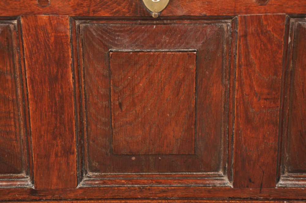 An 18th-century dark oak coffer bach with a hinged lid, three front panels, two lower drawers, and brass handles. View XII