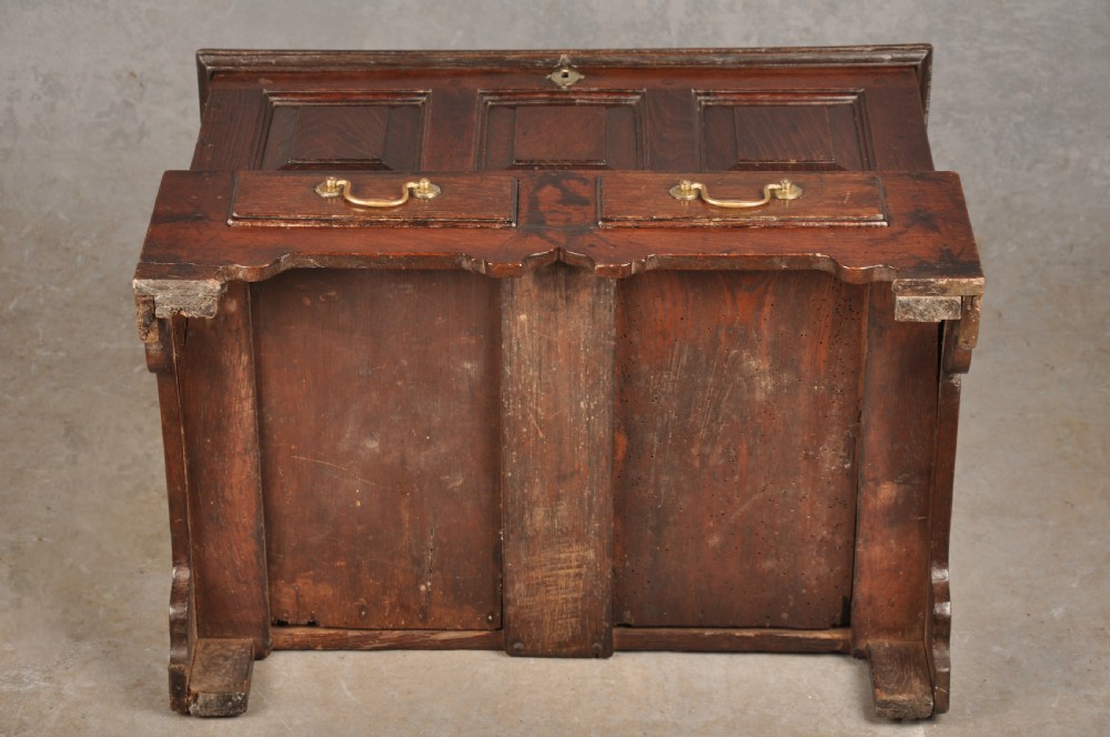 An 18th-century dark oak coffer bach with a hinged lid, three front panels, two lower drawers, and brass handles. View XIII