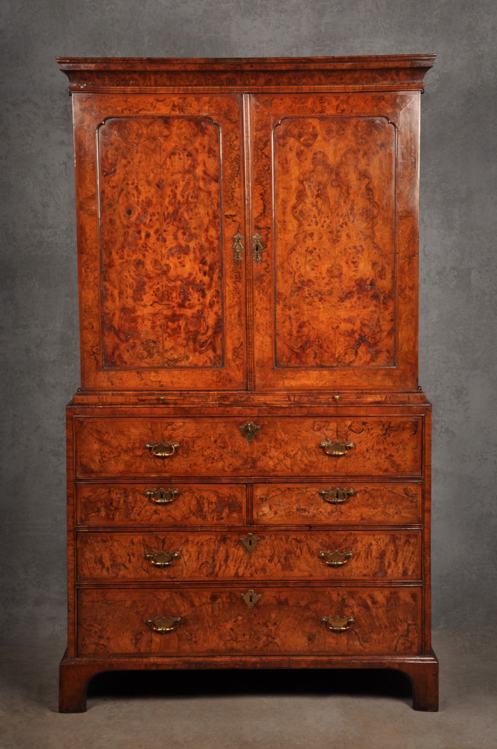 An early eighteenth-century burr walnut secretaire cabinet featuring double upper doors and a lower chest of drawers with brass handles. View II