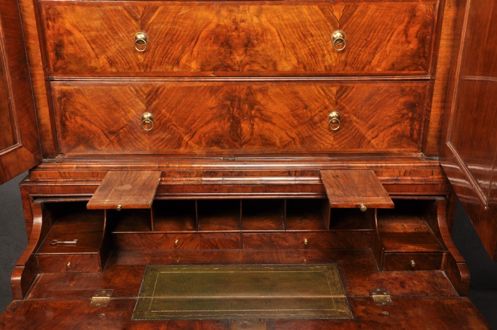 An early eighteenth-century burr walnut secretaire cabinet featuring double upper doors and a lower chest of drawers with brass handles. View XVIII