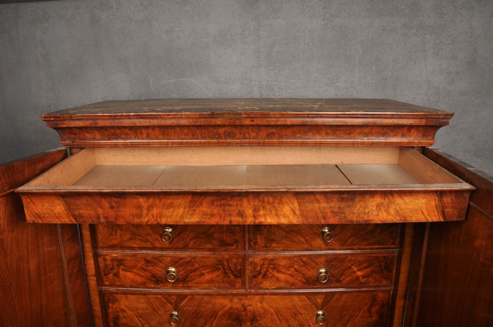 An early eighteenth-century burr walnut secretaire cabinet featuring double upper doors and a lower chest of drawers with brass handles. View XXVII