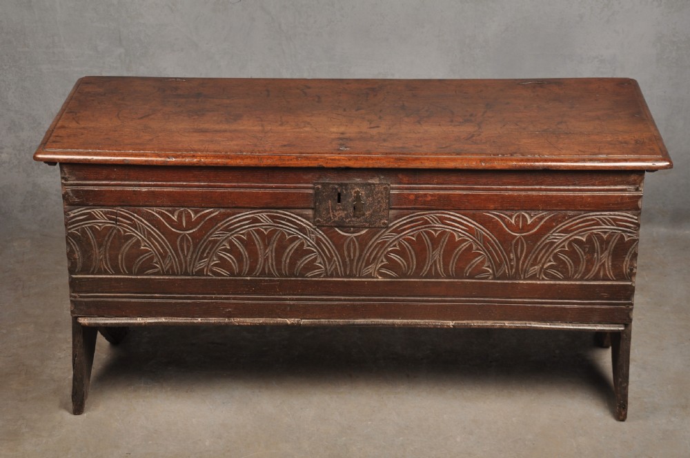 A small 17th century dark oak coffer featuring a flat hinged lid, carved lunette motifs across the front panel, and an iron lock plate.