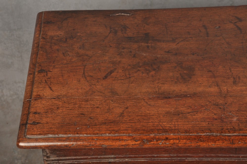 A small 17th century dark oak coffer featuring a flat hinged lid, carved lunette motifs across the front panel, and an iron lock plate. View V