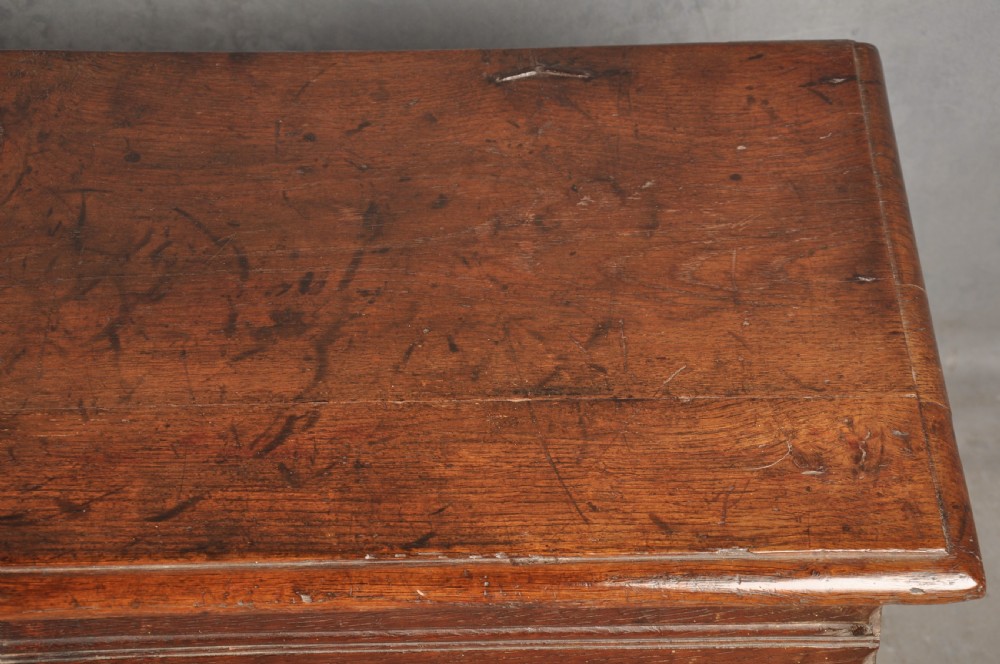 A small 17th century dark oak coffer featuring a flat hinged lid, carved lunette motifs across the front panel, and an iron lock plate. View VI