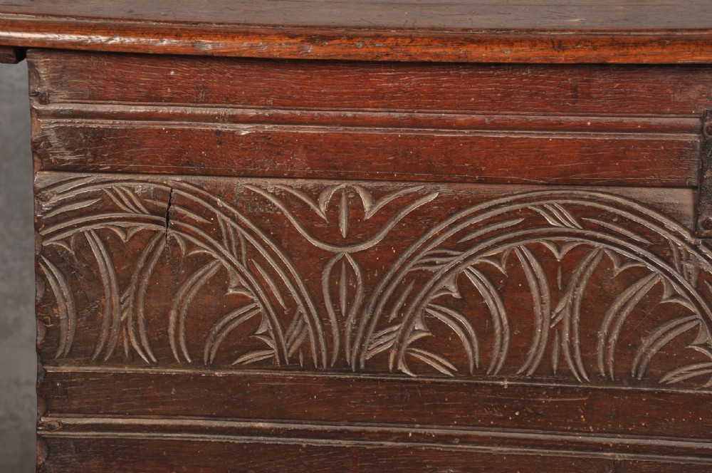 A small 17th century dark oak coffer featuring a flat hinged lid, carved lunette motifs across the front panel, and an iron lock plate. View VII