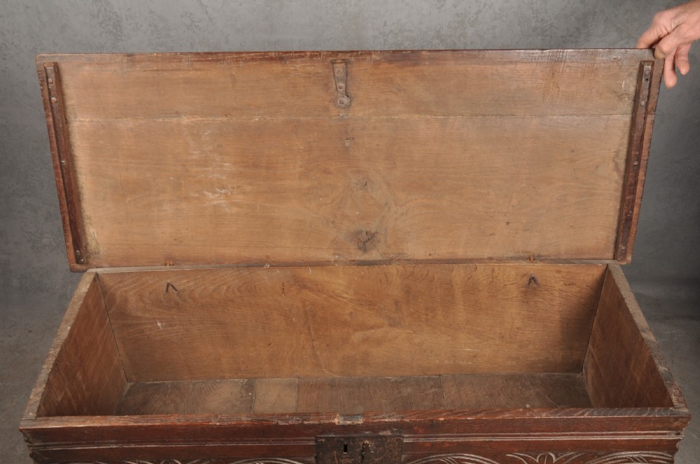 A small 17th century dark oak coffer featuring a flat hinged lid, carved lunette motifs across the front panel, and an iron lock plate. View IX