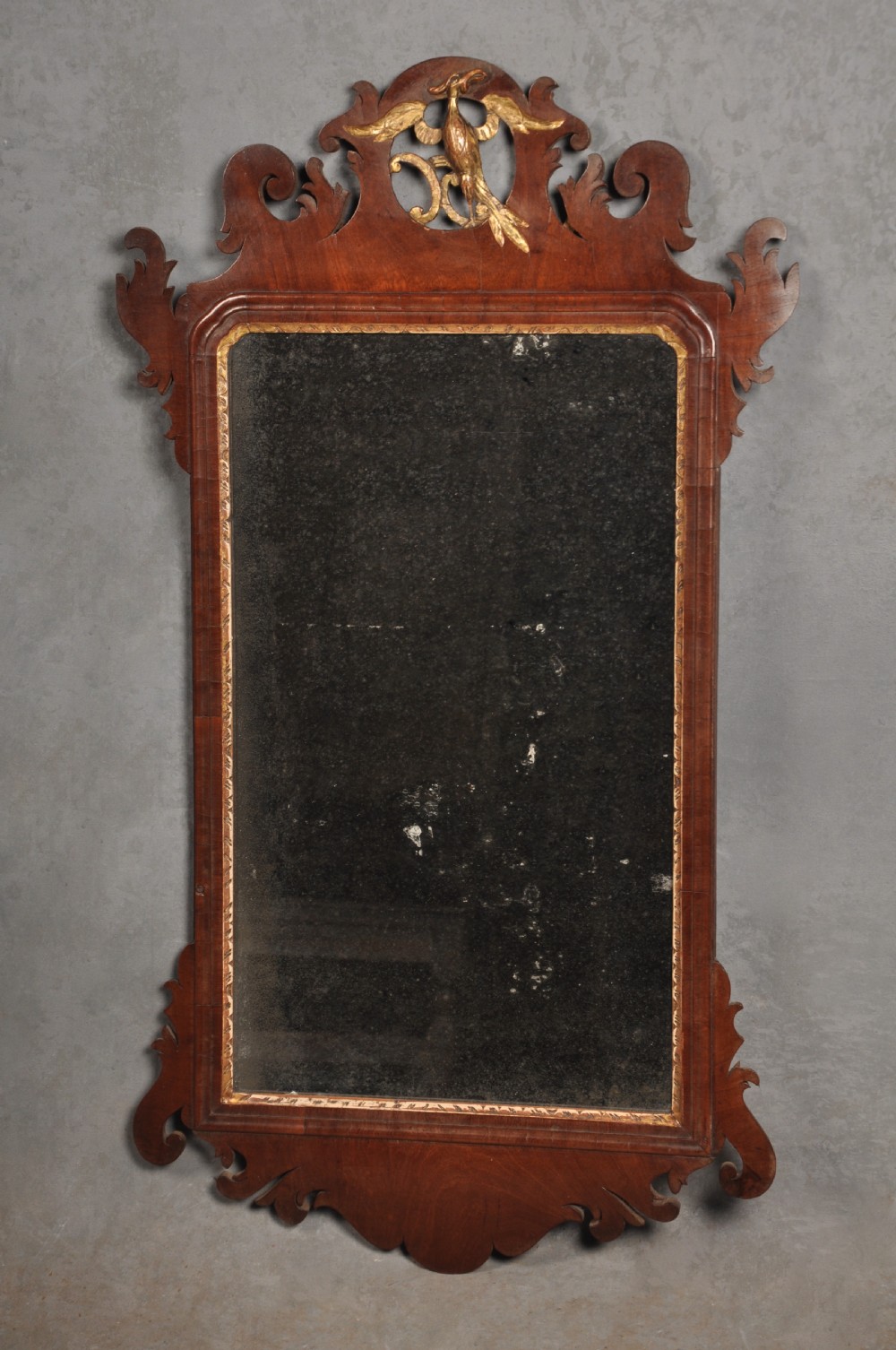 An 18th-century Chippendale style wall mirror featuring a fretwork mahogany frame, a gilded inner moulding, and a gilt phoenix crest at the top.