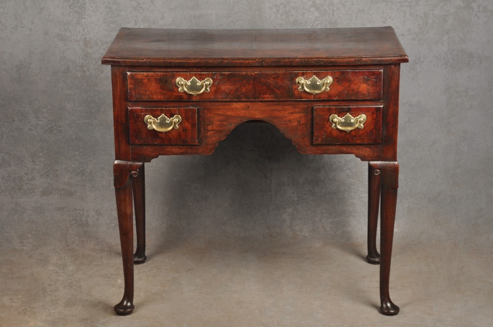 An 18th-century George II mahogany lowboy with three drawers, brass handles, a central arch apron, and four cabriole legs ending in pad feet.