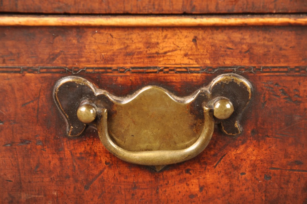 An early 18th-century walnut kneehole desk featuring crossbanded drawer fronts, brass drop handles, a central recessed cupboard, and turned bun feet. View II