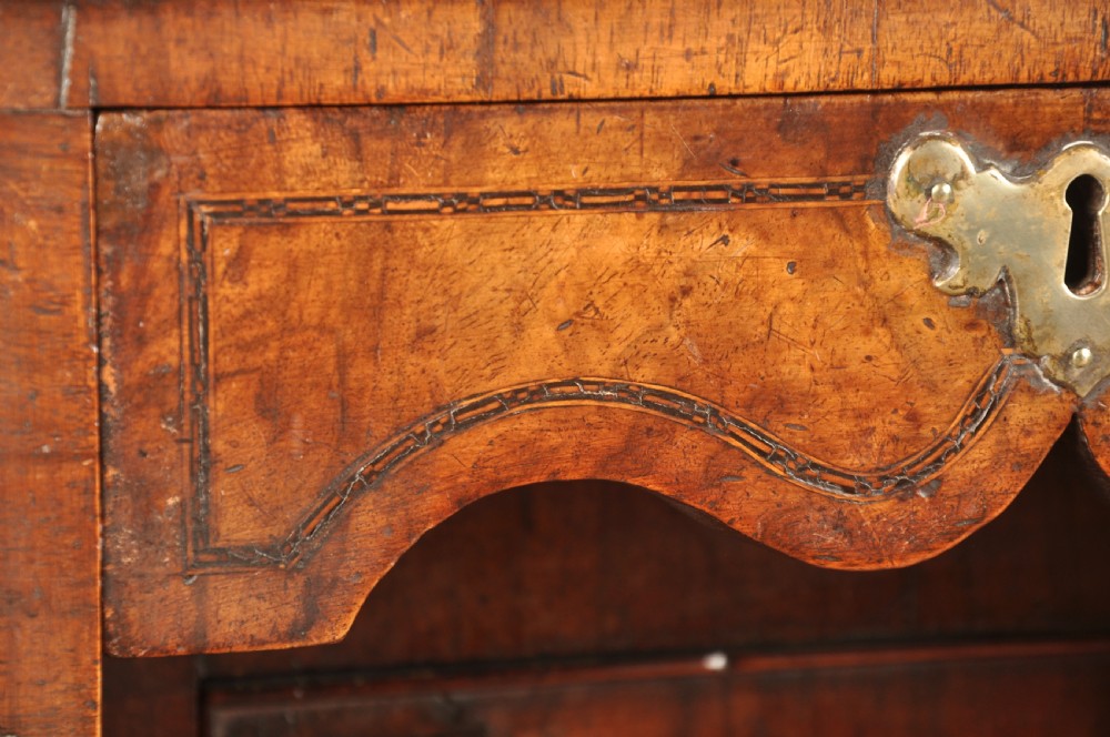 An early 18th-century walnut kneehole desk featuring crossbanded drawer fronts, brass drop handles, a central recessed cupboard, and turned bun feet. View VI
