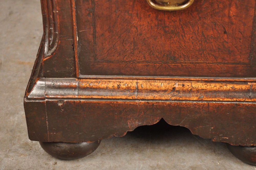 An early 18th-century walnut kneehole desk featuring crossbanded drawer fronts, brass drop handles, a central recessed cupboard, and turned bun feet. View VII