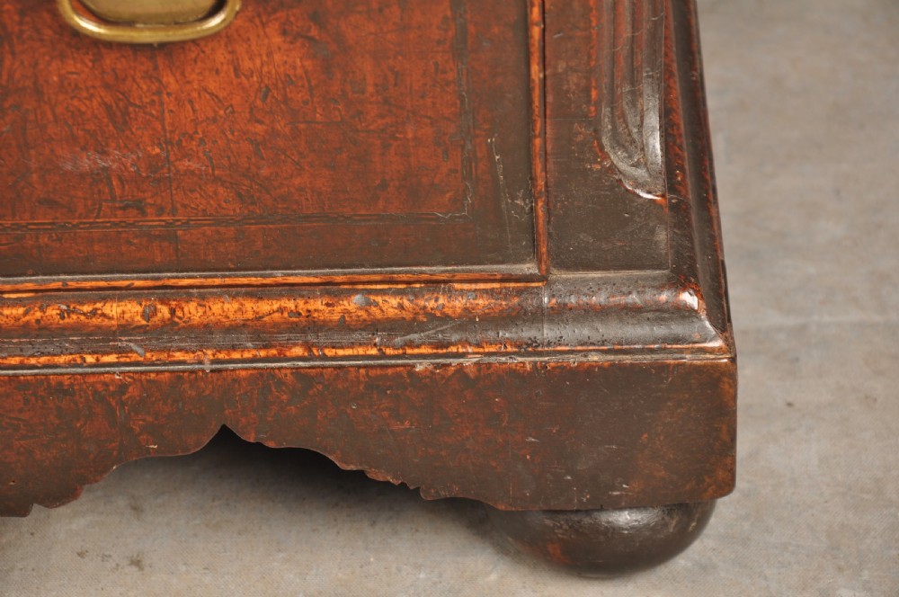 An early 18th-century walnut kneehole desk featuring crossbanded drawer fronts, brass drop handles, a central recessed cupboard, and turned bun feet. View IX