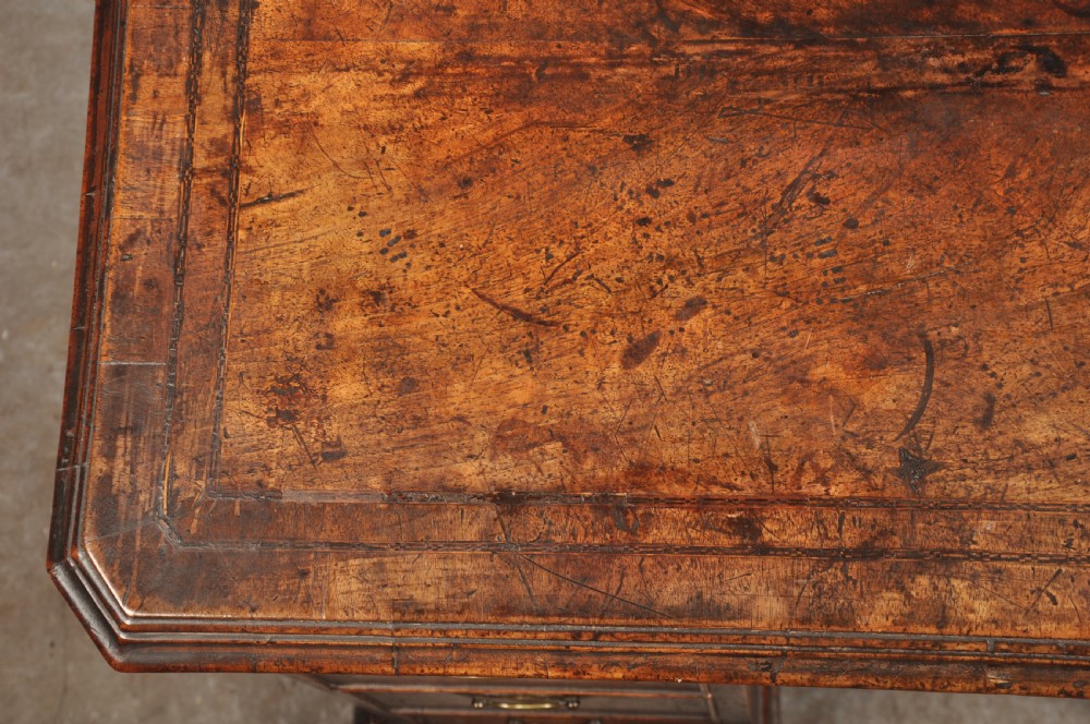 An early 18th-century walnut kneehole desk featuring crossbanded drawer fronts, brass drop handles, a central recessed cupboard, and turned bun feet. View XV